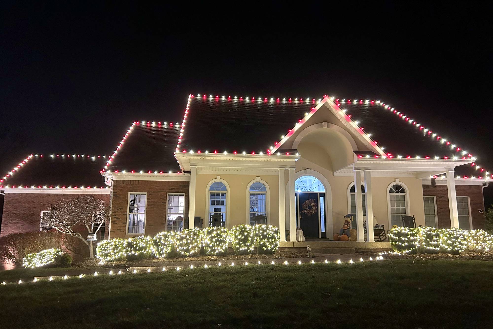 Red and warm white alternating Christmas roofline lights with lit bushes and a lit wreath in Middletown, Kentucky, installed by Louisville Christmas Light Pros